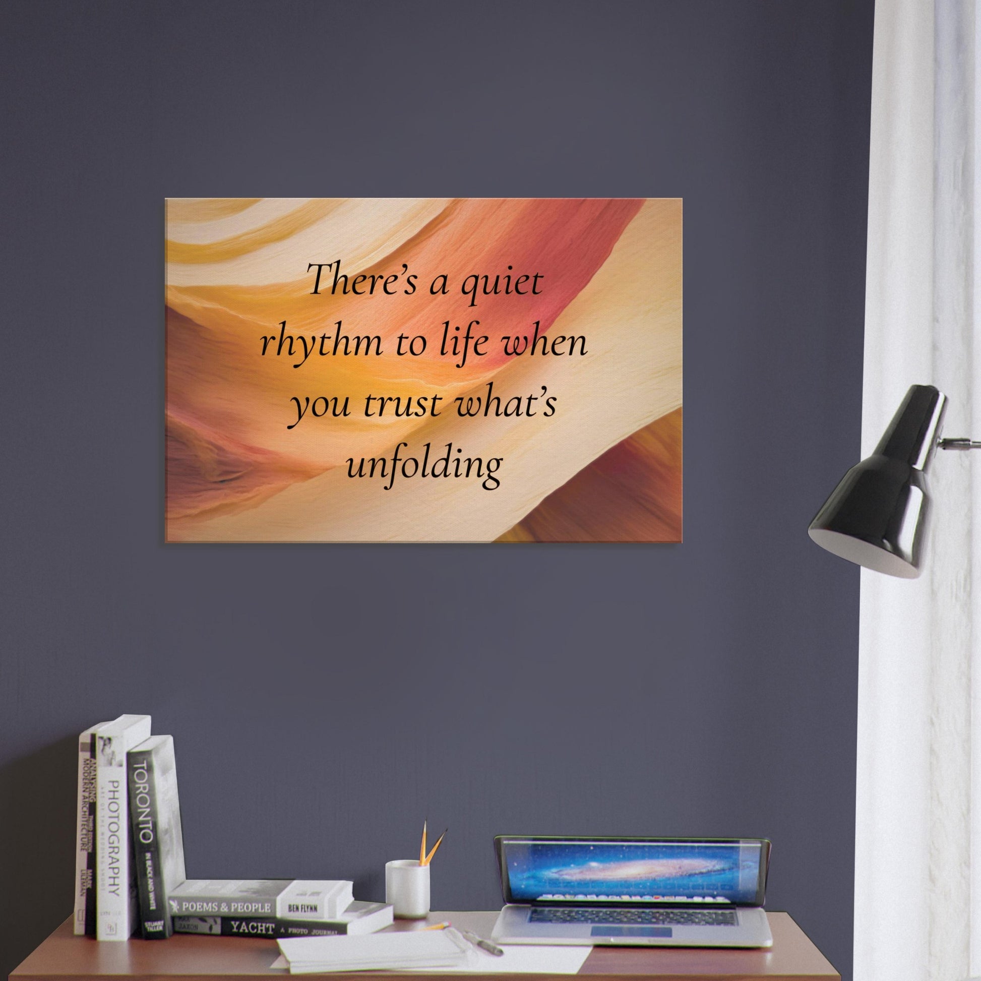 Canvas art with a quote "There's a quiet rhythm to life when you trust what's unfolding" on an abstract background with warm red, cream and caramel colors.  This spiritual canvas print is hung on a dark purple wall in an office decor setting.  
