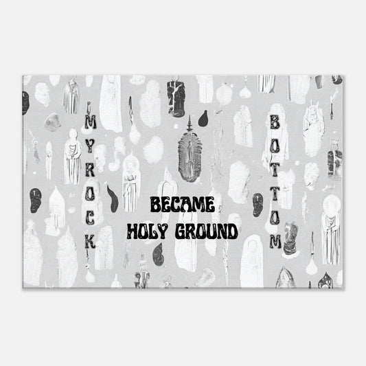 Canvas wall art with quote "My Rock Bottom Became Holy Ground" on top of a white and gray image of holy figures.  This faith based spiritual art is placed on a white back wall. 