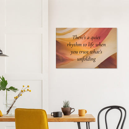 Canvas art with a quote "There's a quiet rhythm to life when you trust what's unfolding" on an abstract background with warm red, cream and caramel colors.  This spiritual canvas wall art is hanging on a white wall as decor in a kitchen space. 
